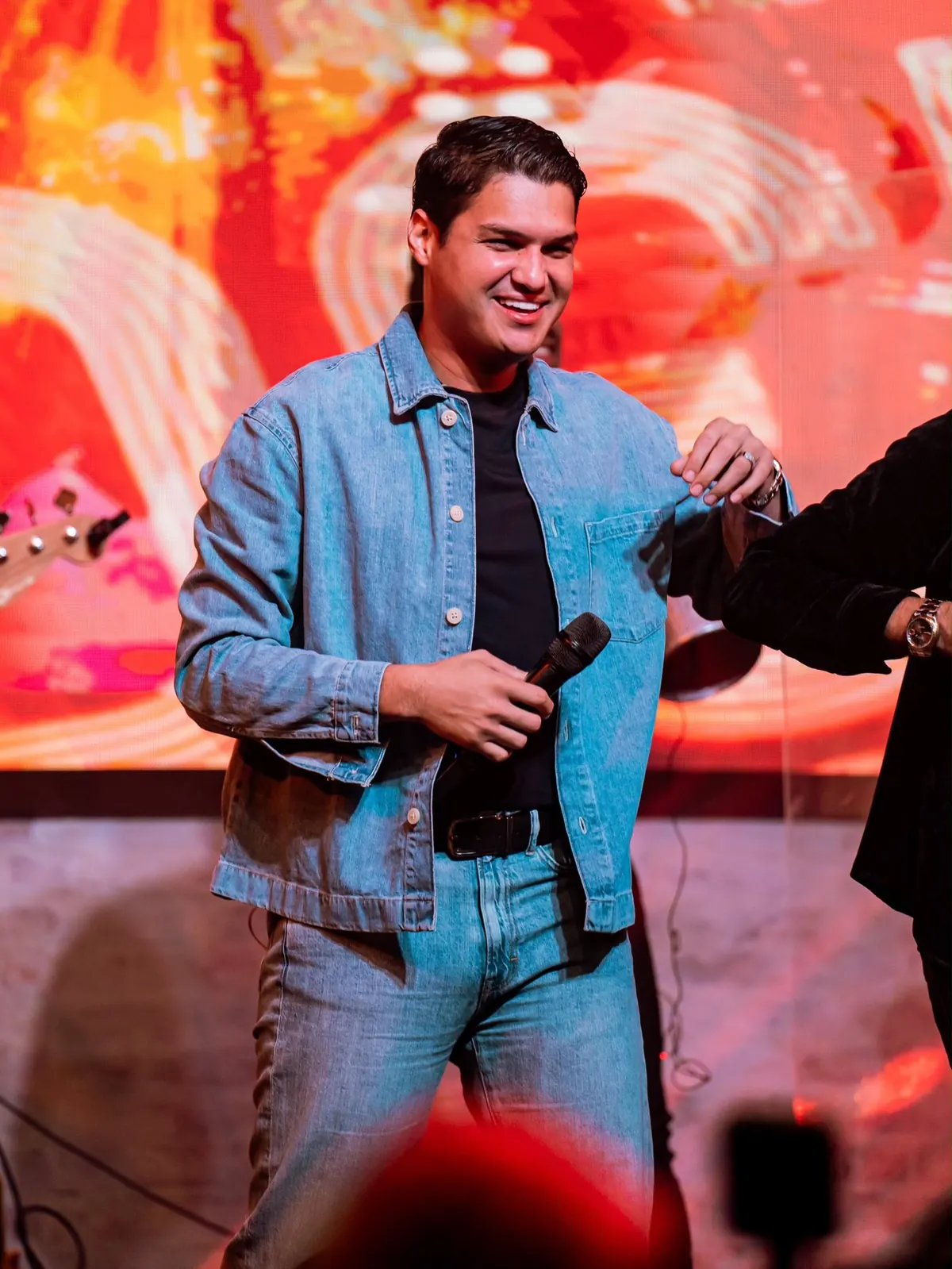 Elder Dayan sonriendo en tarima con chaqueta de jean