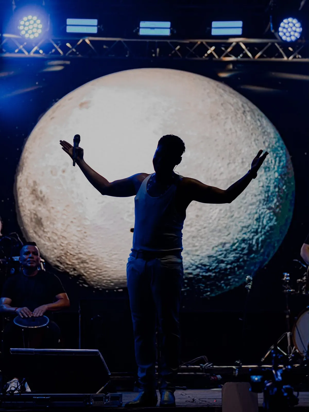 Silueta de Elder Dayan con los brazos abiertos frente a una luna gigante